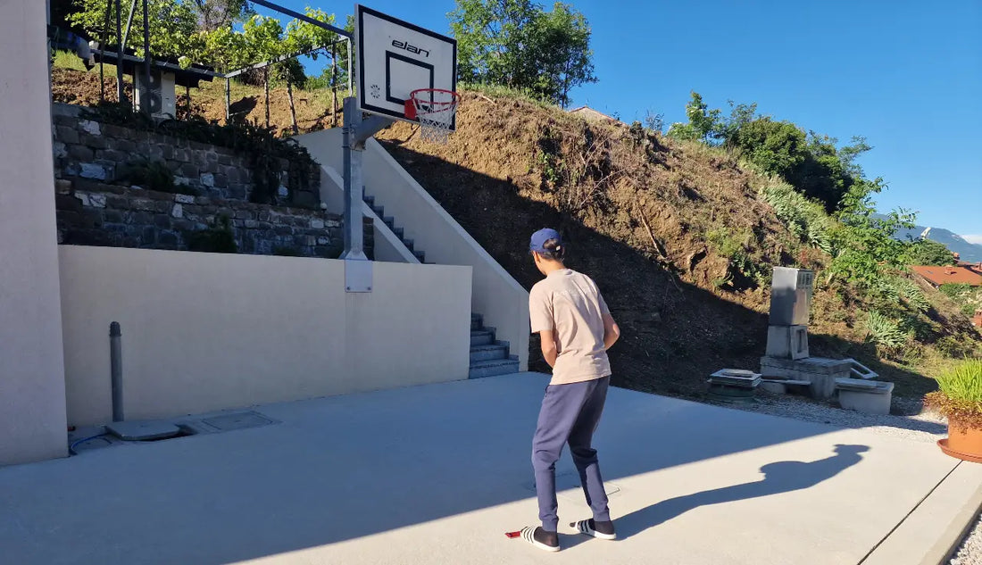 Person playing basketball on an outdoor court with mountains in the background.