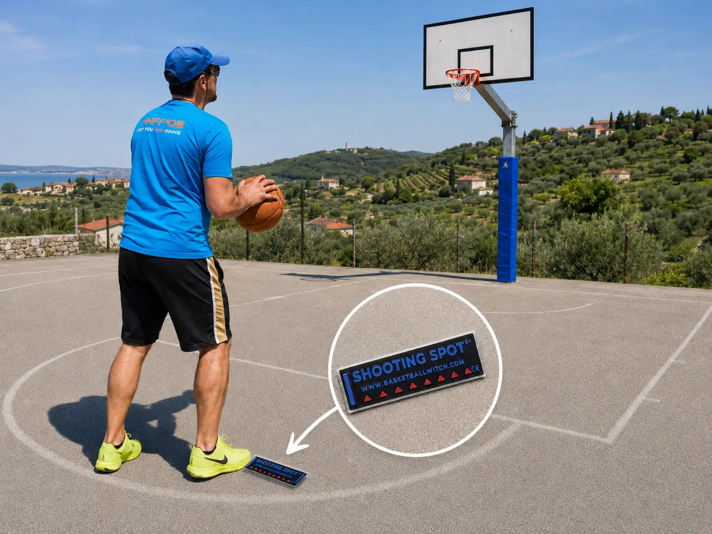 Basketball Witch black, blue and red Shooting Spot Marker on an outdoor basketball court, highlighted under a player’s foot with a hoop and Slovenian coastal countryside in the background.