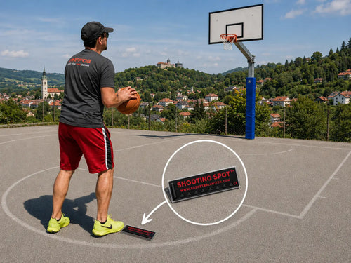 Outdoor basketball scene showing the Basketball Witch black and red Shooting Spot Marker placed on a court near a player, with a hoop and scenic Novo Mesto hills in the background.
