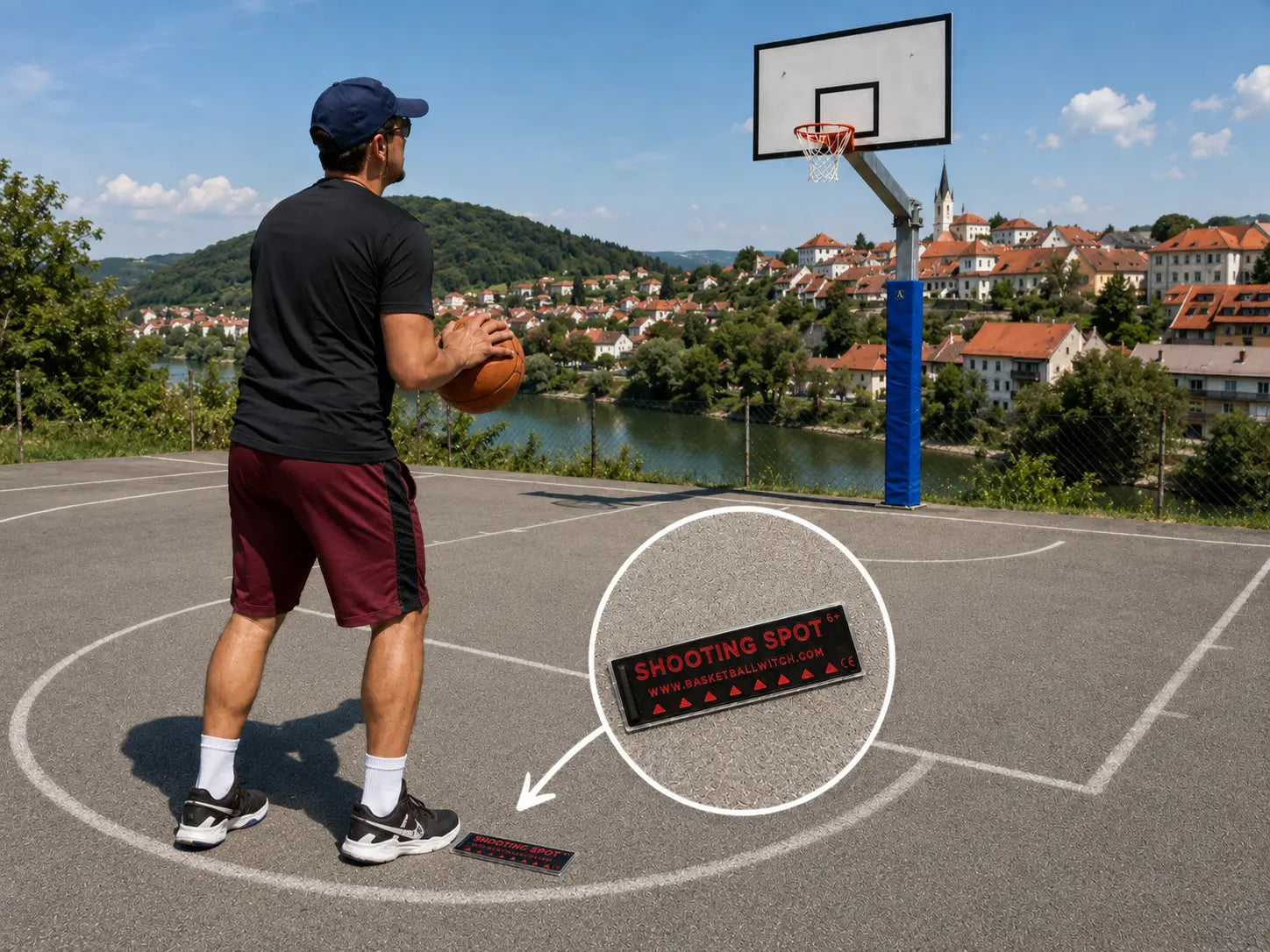 Basketball Witch black and red Shooting Spot Marker on an outdoor basketball court, highlighted near a player preparing to shoot with a hoop and Novo mesto landscape in the background.