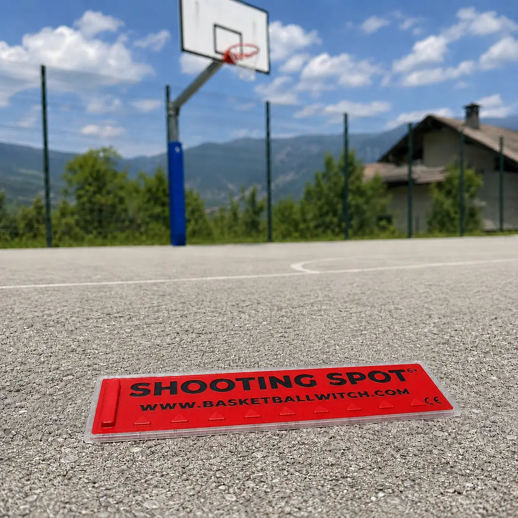 Red Shooting Spot marker on a basketball court with a basketball hoop in the background.